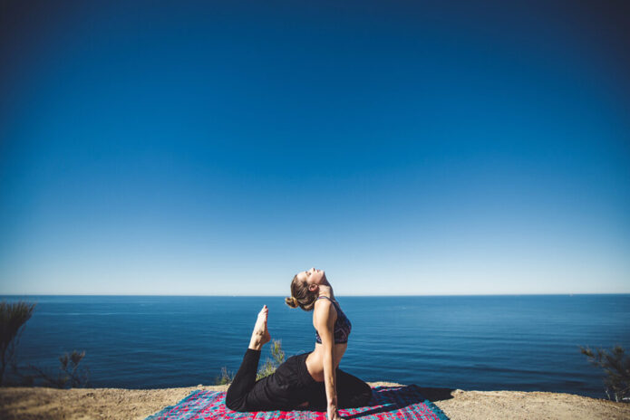 A woman doing yoga on top of a rock near the ocean, benefiting from nutritional IV therapy.