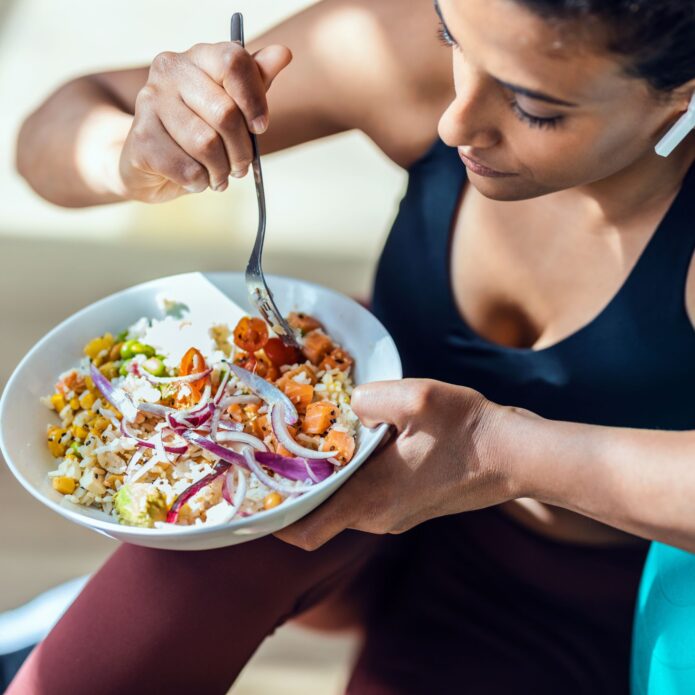 A woman receiving nutritional IV therapy while eating a bowl of salad.