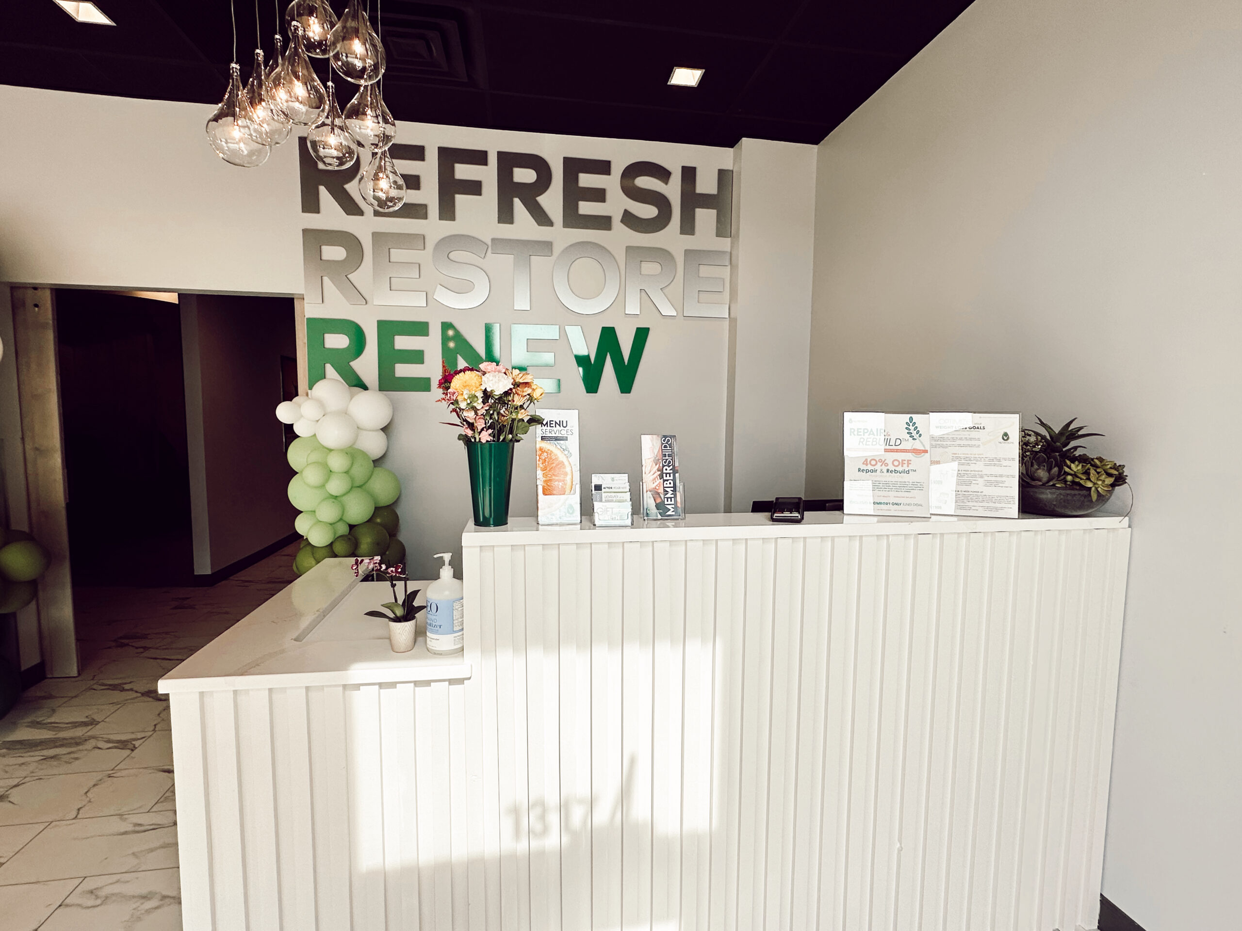 A reception area with a sign that says refresh restore renew, offering drip hydration and blood testing services.