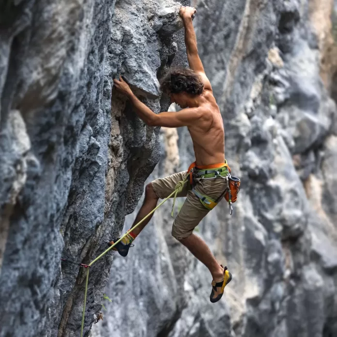 Climber ascending a steep rock face using ropes for safety.