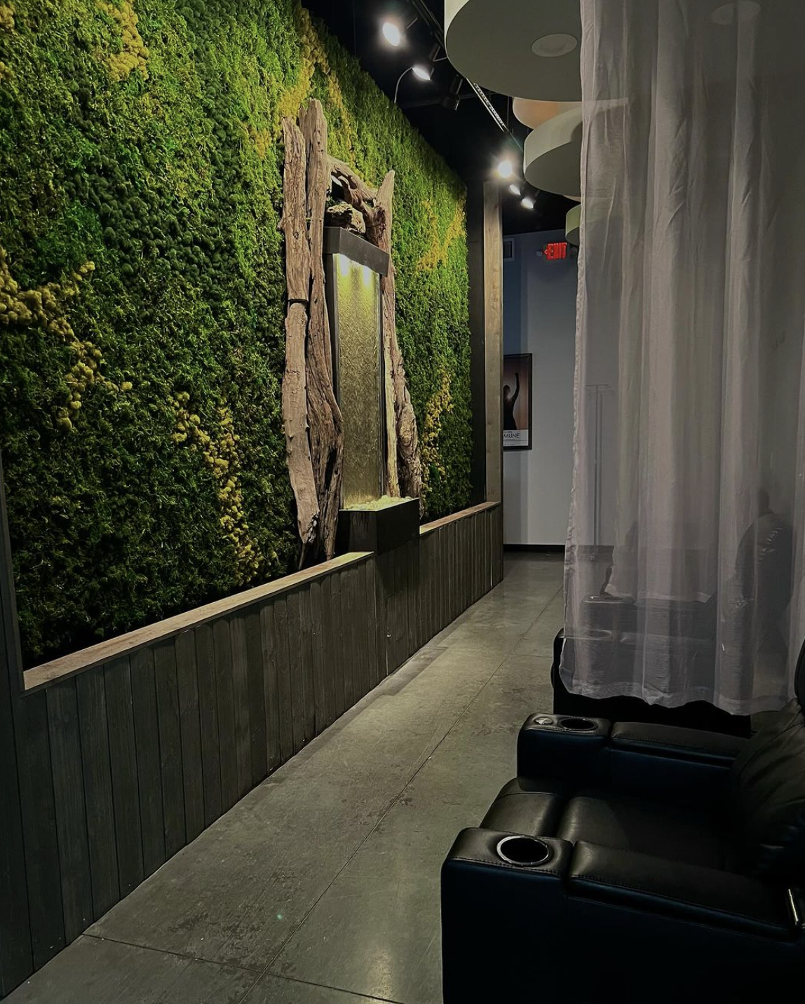 An indoor space with a vertical garden wall and a water feature, accompanied by black lounge chairs and sheer curtains.