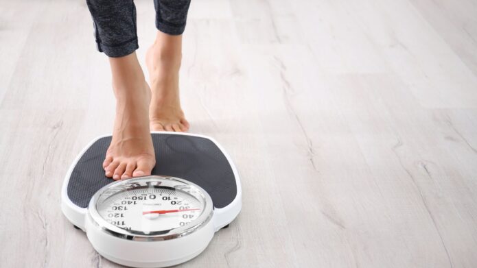 A person standing on a bathroom scale displaying weight in pounds.